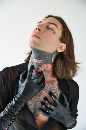 vertical shot of sexy man with tattoos in transparent shirt with hands in leather gloves on neck