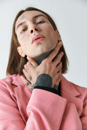 stylish young male model with tattoos in pink blazer looking at camera with hands on neck, fashion