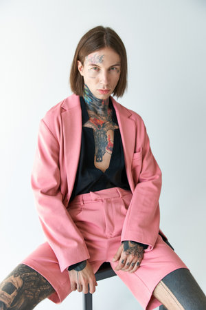 handsome man in stylish outfit with tattoos sitting on chair and looking at camera, fashion conceptの写真素材