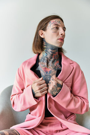 vertical shot of alluring young man with tattoos sitting on comfy chair looking away, fashionの写真素材