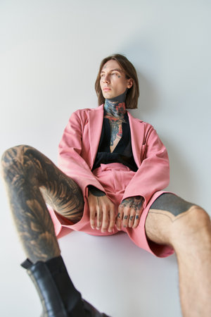 good looking young man with tattoos and piercing in pink blazer looking away, fashion conceptの写真素材