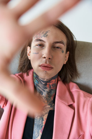 vertical shot of handsome young man with tattoos sitting on chair with hand in front of cameraの写真素材