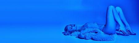 appealing woman in erotic lingerie and faux fur lying on floor surrounded by blue lights, bannerの写真素材