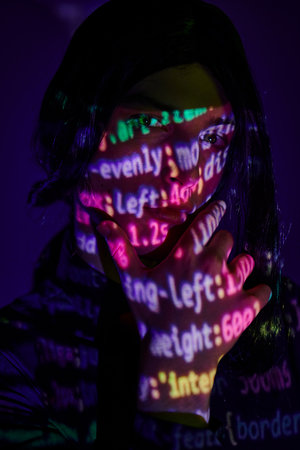 anime style student looking at camera in neon light with programming symbols on dark blueの写真素材