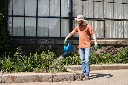 handsome and bearded gardener in sun hat holding watering can and shovel in countrysideの写真素材
