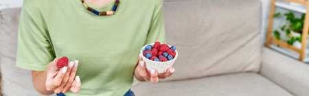 cropped view of female vegetarian with blueberries and raspberries in living room, horizontal banner