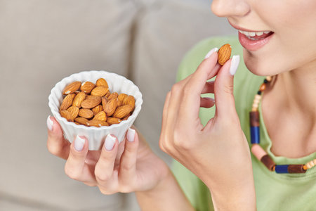 partial view of young woman with white ceramic bowl of almonds, delicious vegetarian diet conceptの写真素材