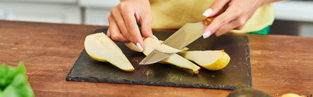 cropped view of vegetarian woman cutting ripe pear on chopping board in kitchen, horizontal bannerの写真素材