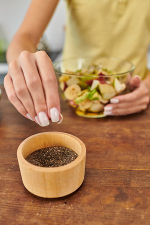 cropped vegetarian woman taking sesame seeds from wooden bowl while preparing fruit salad at homeの写真素材