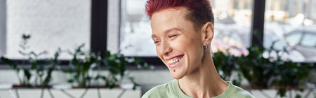 stylish and cheerful non-binary individual with short hair laughing in office, horizontal bannerの写真素材