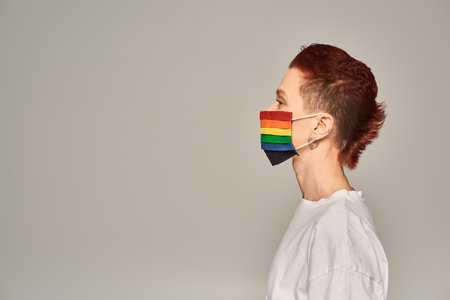 side view of redhead queer person in rainbow colors medical mask on grey backdrop, profile portraitの写真素材