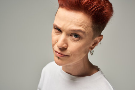 skeptical and suspicious redhead non-binary person looking at camera on grey studio backdrop