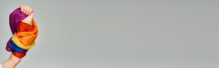 cropped view of hand of non-binary person holding LGBT flag on grey backdrop, banner with copy spaceの写真素材