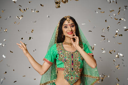 joyous young indian woman in national clothes with bindi and green veil surrounded by confettiの写真素材