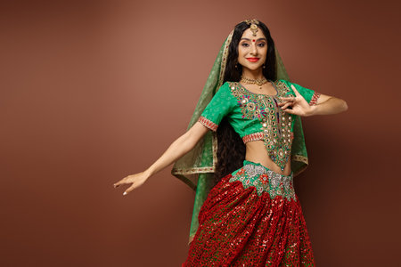 cheerful young indian woman in green choli with bindi dot gesturing while dancing looking at cameraの写真素材