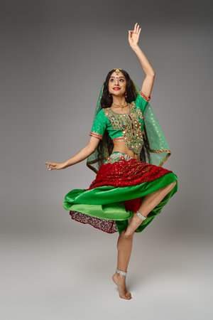 young indian woman in national attire standing on one leg with arm raised while dancing activelyの写真素材