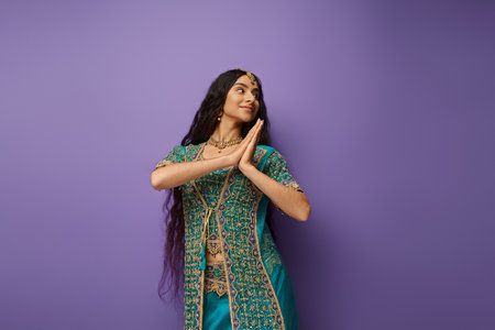 pretty joyful indian woman in blue sari with accessories posing in motion on purple backdrop