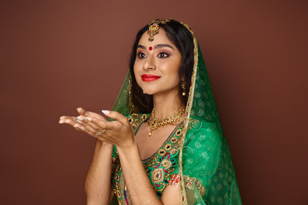 beautiful young indian woman in traditional clothes posing with open palms and looking awayの写真素材