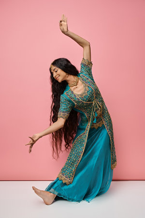 beautiful indian woman in traditional clothes gesturing while dancing actively on pink backdrop