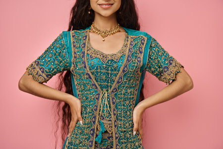 cheerful young indian woman in national costume posing with arms akimbo and smiling joyfully,...