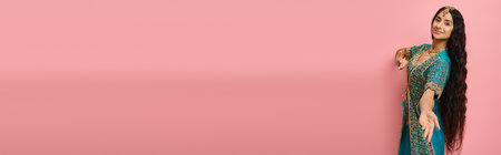 beautiful female model in blue traditional sari looking at camera posing on pink backdrop, banner