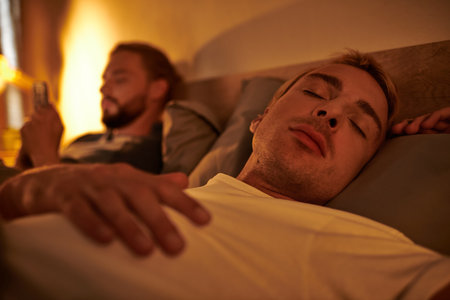 gay man sleeping near unfaithful boyfriend browsing date app on smartphone at night in bedroom