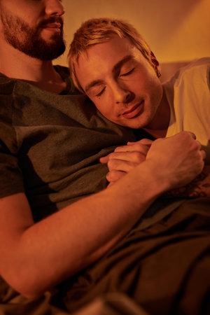 tattooed gay man sleeping on chest of bearded boyfriend at night in bedroom, love and serenity