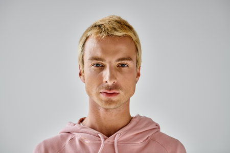 portrait of charismatic man with dyed blonde hair looking at camera on grey backdrop, modern styleの写真素材