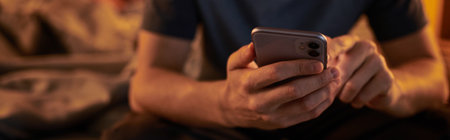 cropped view of adult man using mobile phone in bedroom at home at nighttime, horizontal bannerの写真素材