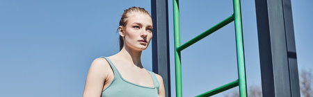 banner of young blonde woman in crop top standing near vertical ladder outside in sunny day