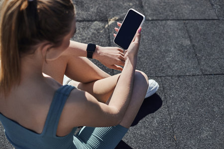 top view of fit woman in activewear with fitness tracker on wrist using smartphone after workoutの写真素材