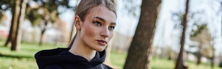 portrait of sporty young woman in black hoodie looking away in green park, nature and sport bannerの写真素材