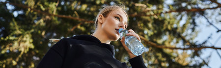 banner of young woman with blonde hair and sportswear drinking water after working out in park