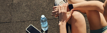 banner of sportswoman in activewear checking fitness tracker next to smartphone and water bottle