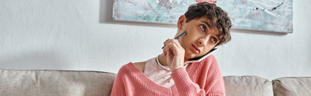 transgender blogger in pink sweater talking on smartphone and holding pen, horizontal banner