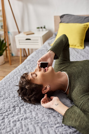 happy and curly transgender person in casual attire talking on smartphone in bedroom, phone callの写真素材