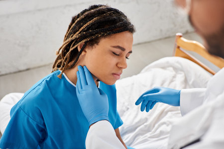 sick pretty african american woman closing eyes while her indian doctor examining her lymph nodesの写真素材