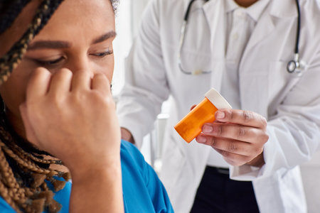 focus on pills in hands of indian doctor next to blurred depressed african american patientの写真素材