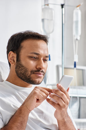 concentrated indian patient lying in hospital bed in his ward with phone in hands, healthcareの写真素材
