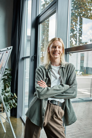 cheerful long haired androgynous person in business attire with crossed arms smiling at cameraの写真素材