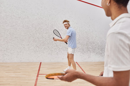 focus on happy man in sportswear playing with african american friend inside of squash courtの写真素材