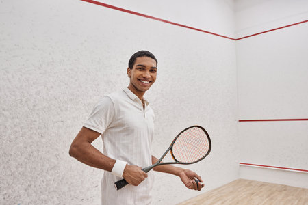 happy african american man in active wear holding squash ball and racquet while playing in courtの写真素材