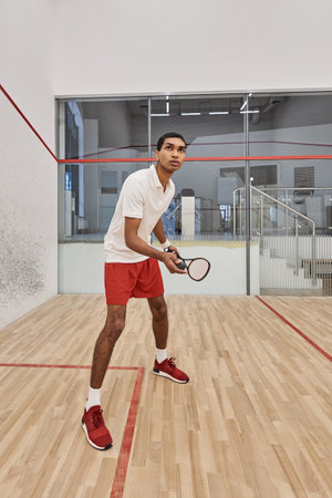 vertical shot of african american sportsman holding squash ball and racquet while playing gameの写真素材