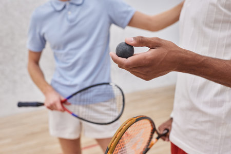 cropped view of african american man holding squash ball near friend inside of court, playersの写真素材