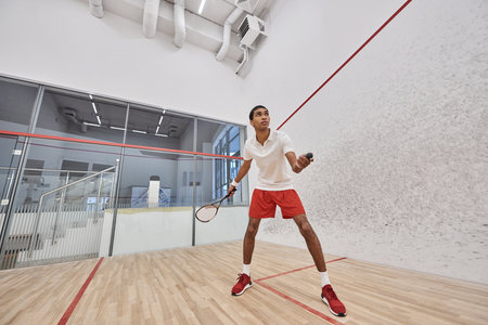 fit african american sportsman holding squash ball and racquet while playing game inside of courtの写真素材