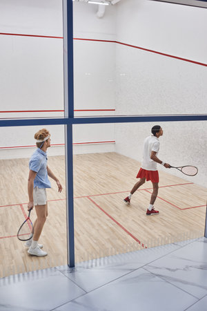 multicultural friends in sportswear playing squash together inside of court, motivation and sportの写真素材
