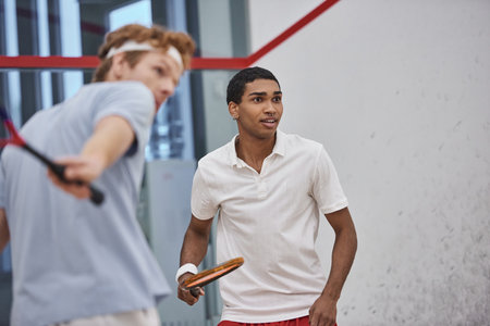 excited african american man holding squash racquet while playing with friend on blurred foregroundの写真素材