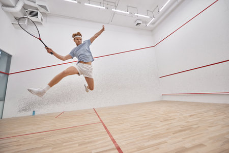 motion shot, active player holding racquet and jumping while playing squash inside of courtの写真素材