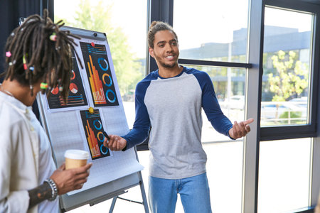 stylish african american manager talking near flip and colleague with coffee to go in office
