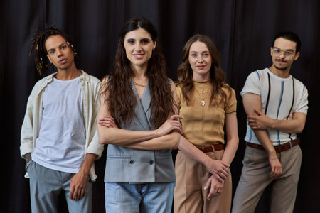 portrait of happy female team lead with folded arms near multiethnic team on black in officeの写真素材